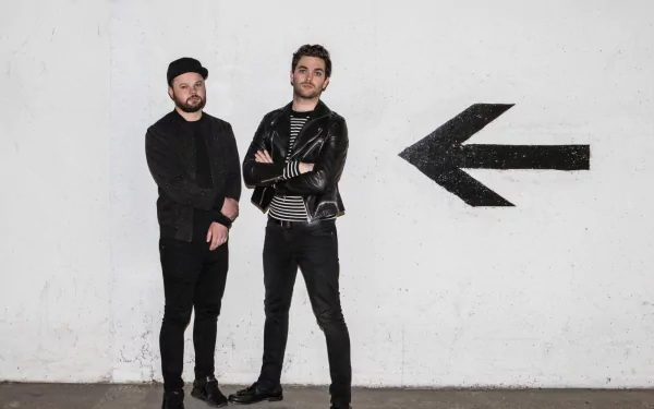 HD wallpaper of two band members from Royal Blood standing against a white wall with a large black arrow pointing left.