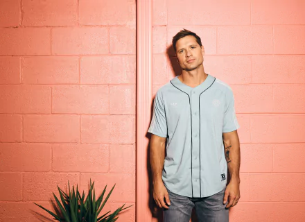 Walker Hayes leans casually against a bright pink wall, wearing a light blue jersey. This HD wallpaper captures a vibrant, music-inspired moment.