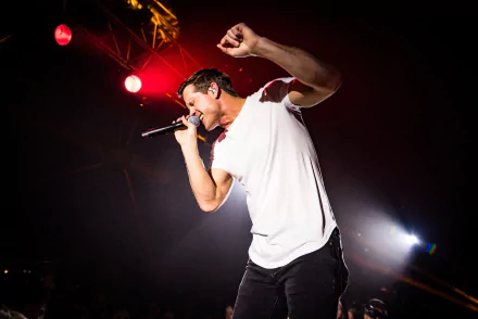 Energetic performer on stage captured in an HD desktop wallpaper, with bright stage lights in the background creating a dynamic concert atmosphere.