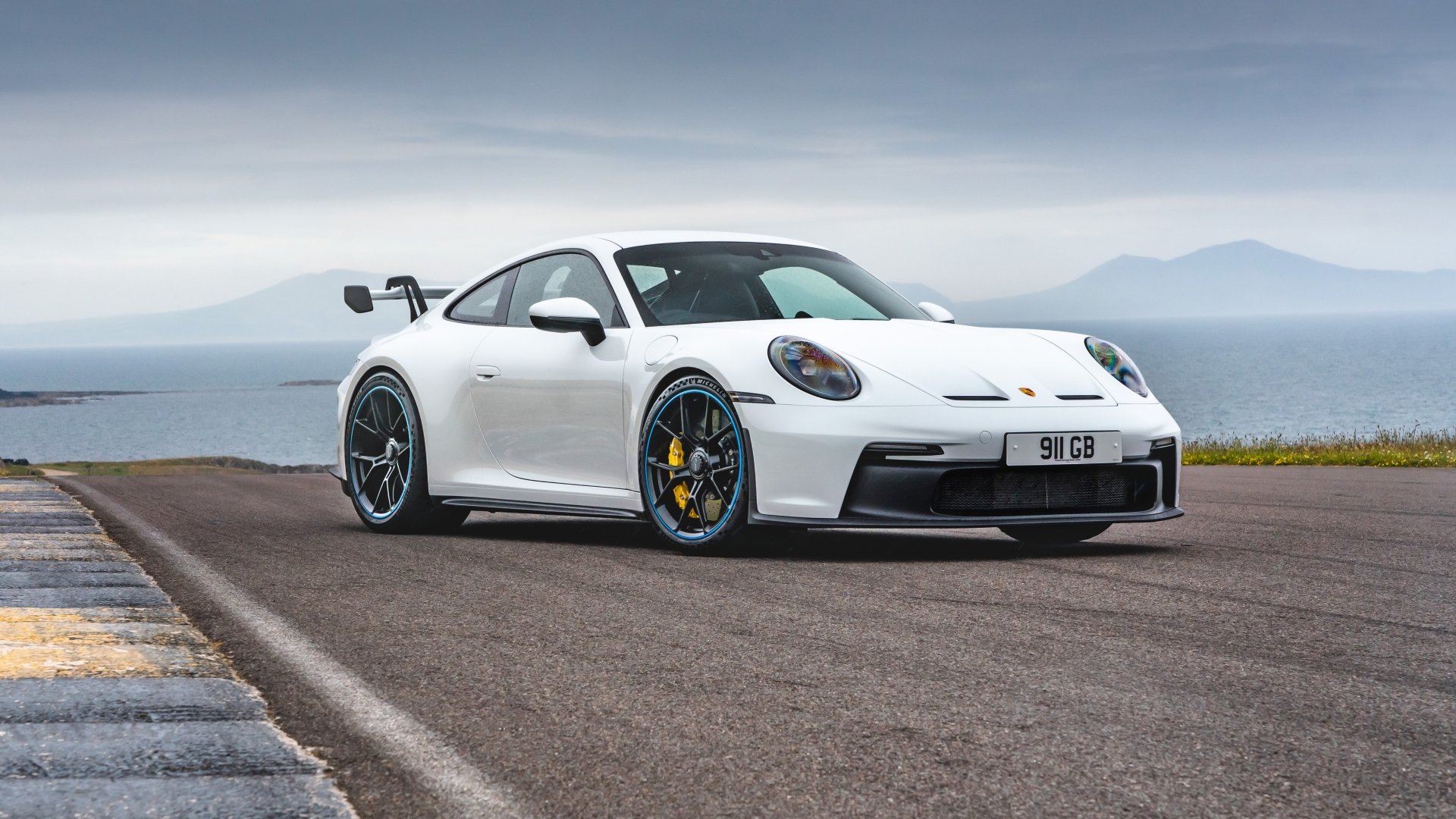 White Porsche 911 GT3 on a coastal road, 5K Ultra HD PC desktop wallpaper background showcasing the Porsche 911 sports vehicle.