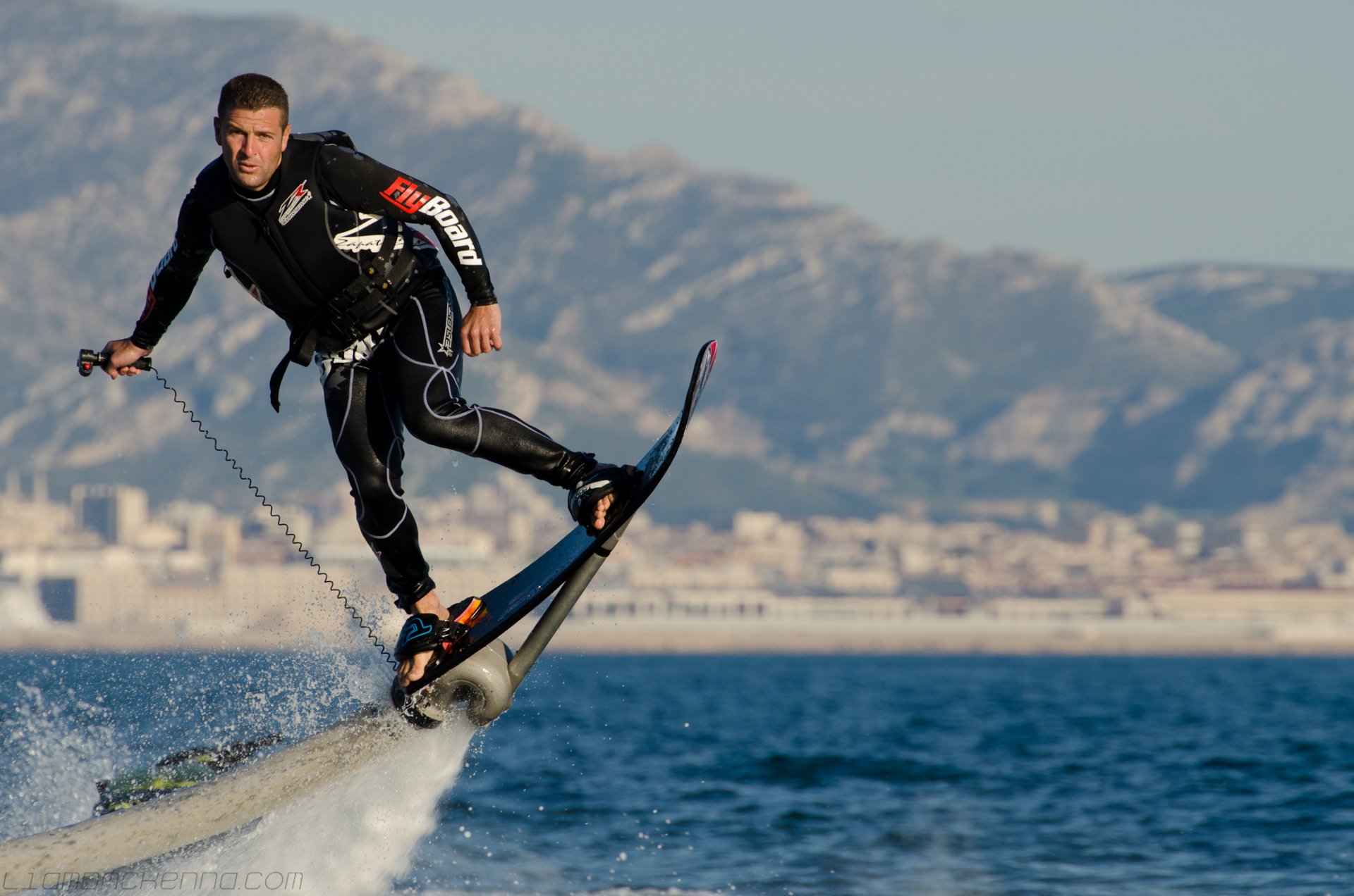 HD desktop wallpaper of a person riding a flyboard above the sea with mountains in the background.