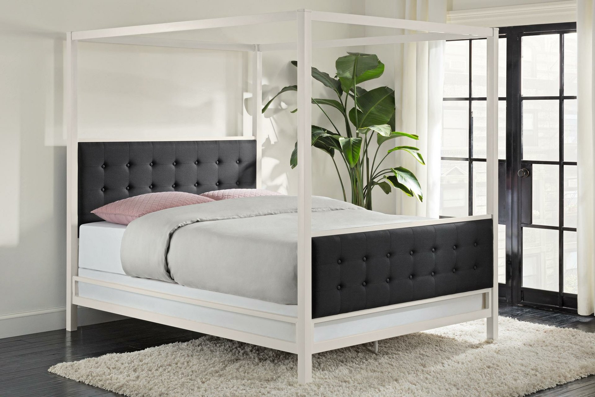 A stylish black and white bed frame with a tufted headboard, complemented by soft bedding and a lush plant, set against large windows, creating a modern bedroom atmosphere.