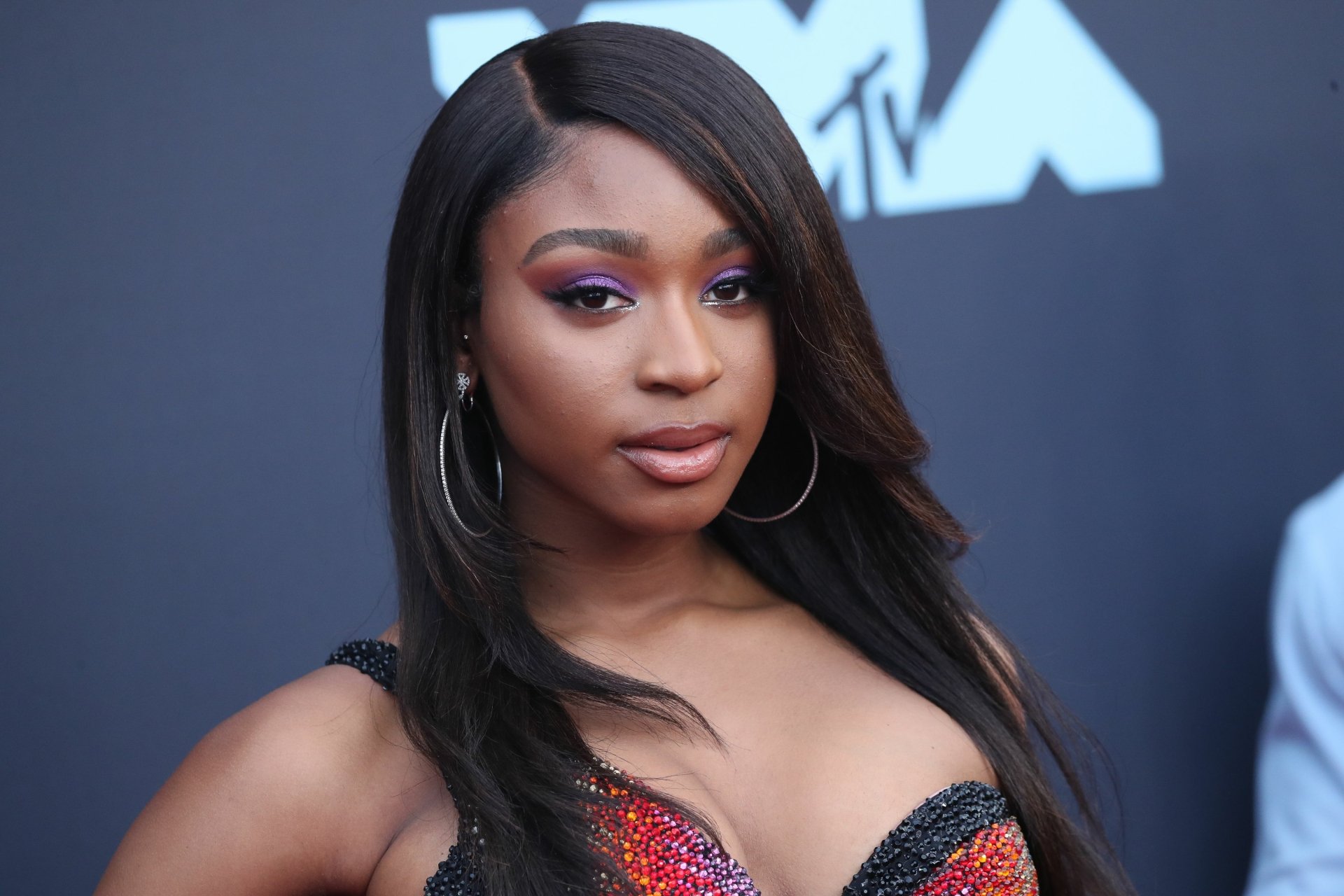 An HD desktop wallpaper featuring Normani, a music artist, showcasing her stylish look at a red carpet event. Her long hair and confident pose draw attention.