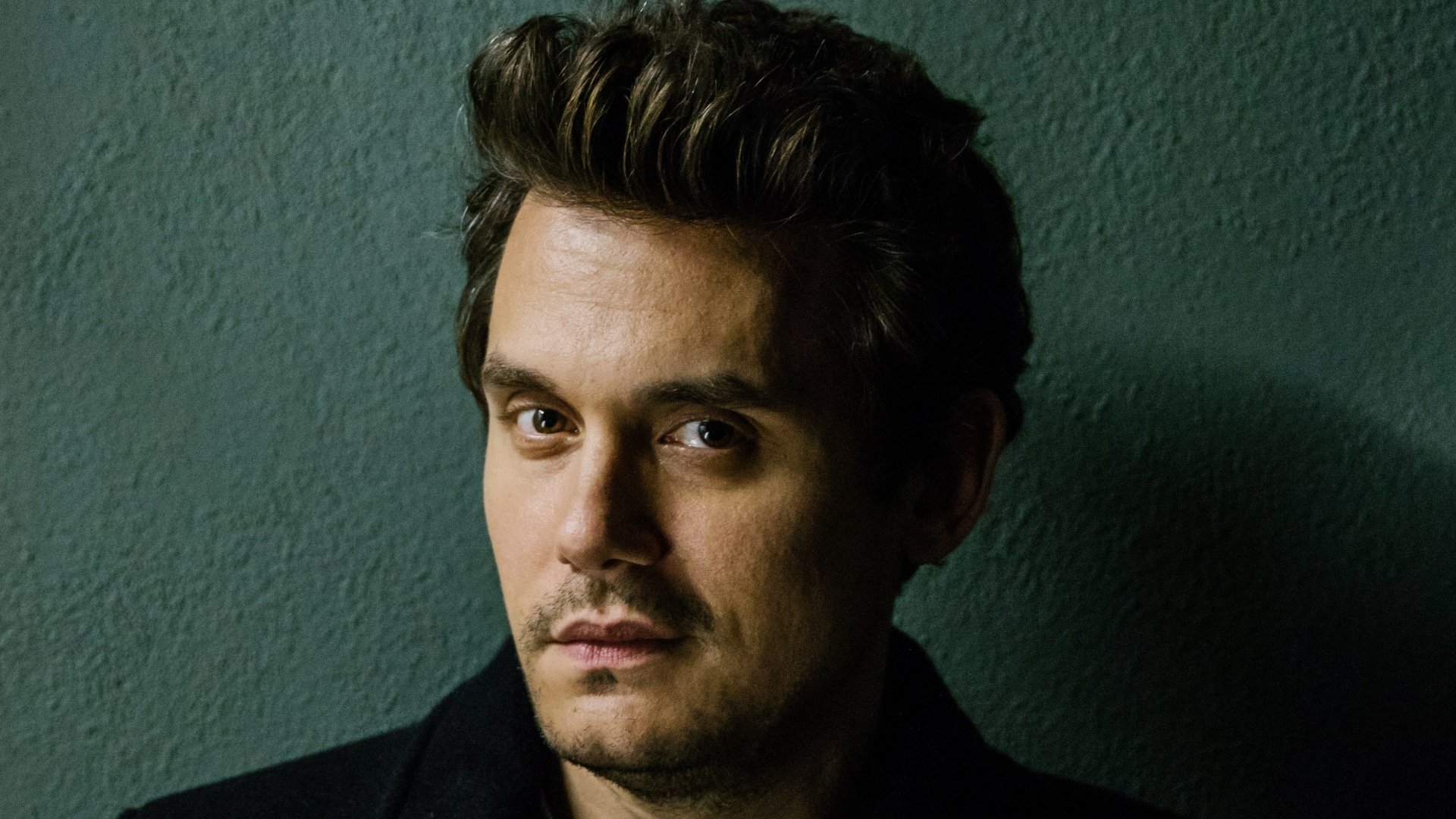 HD desktop wallpaper featuring a close-up portrait of a contemplative man with styled hair, wearing a dark jacket against a textured backdrop.