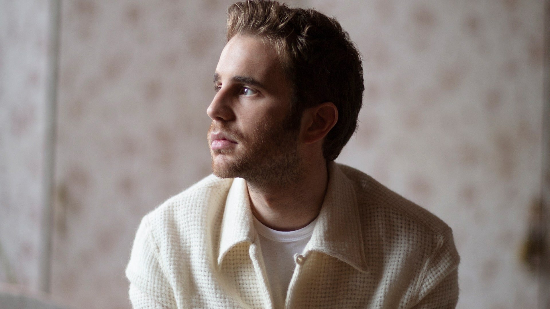 HD desktop wallpaper featuring a contemplative individual in a light-colored jacket, set against a soft, textured background.