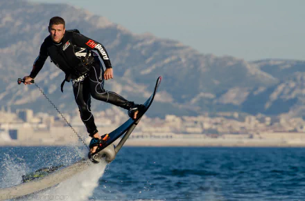 HD desktop wallpaper of a person riding a flyboard above the sea with mountains in the background.