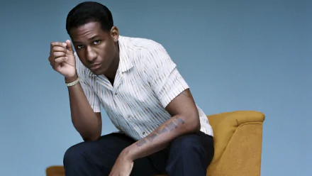 Man in a striped shirt posing on a yellow chair against a blue background, HD desktop wallpaper.