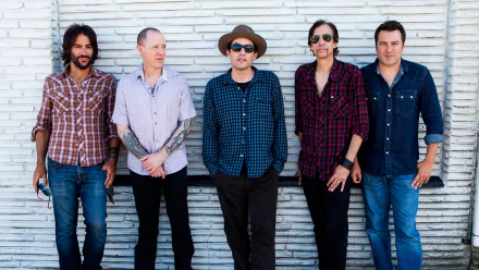 A group of five musicians from The Wallflowers stand confidently against a textured wall, showcasing their varied styles in an engaging HD desktop wallpaper.
