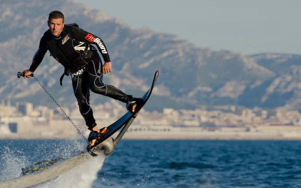 HD desktop wallpaper of a person riding a flyboard above the sea with mountains in the background.