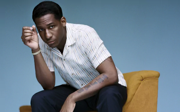 Man in a striped shirt posing on a yellow chair against a blue background, HD desktop wallpaper.