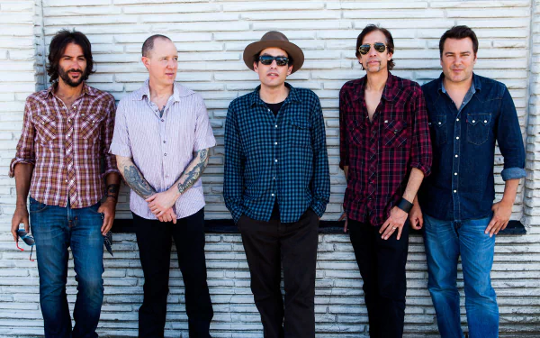 A group of five musicians from The Wallflowers stand confidently against a textured wall, showcasing their varied styles in an engaging HD desktop wallpaper.
