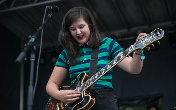 Musician in a striped shirt playing electric guitar on stage, suitable as an HD desktop wallpaper and background.