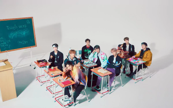 Stray Kids, a K-pop boy band, pose seated at desks in a bright classroom setting, captured in a vibrant 4K Ultra HD PC desktop wallpaper.