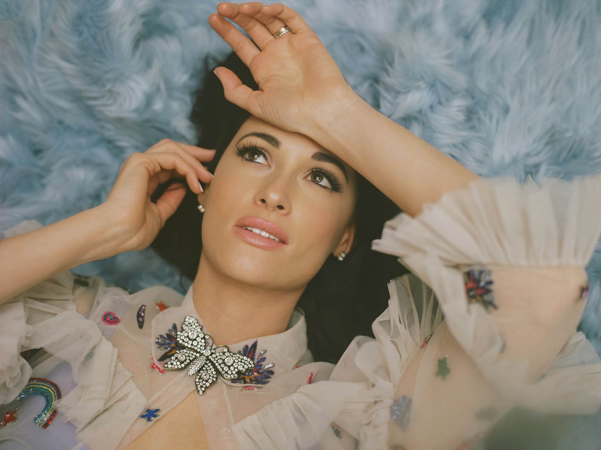 Elegantly dressed woman lying on a blue fluffy background, posing thoughtfully for an artistic HD desktop wallpaper.