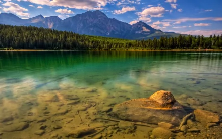 HD desktop wallpaper featuring a tranquil lake with crystal-clear water, forested shoreline, and majestic mountains under a blue sky with scattered clouds. Tags: nature, lake.