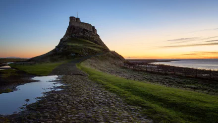 4K Ultra HD desktop wallpaper featuring Lindisfarne Castle, a man-made fortress perched on a rocky hill at sunset with a vibrant sky and tidal landscape.