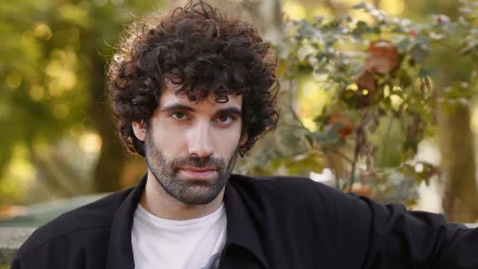 HD desktop wallpaper featuring a curly-haired man in a black jacket with an autumnal background