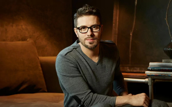 Serene HD wallpaper featuring a man with glasses seated comfortably in a cozy room with warm lighting, providing a stylish background for desktops.