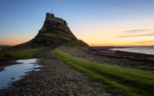 4K Ultra HD desktop wallpaper featuring Lindisfarne Castle, a man-made fortress perched on a rocky hill at sunset with a vibrant sky and tidal landscape.
