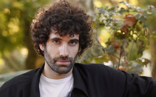 HD desktop wallpaper featuring a curly-haired man in a black jacket with an autumnal background