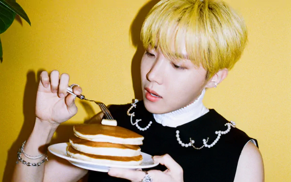 HD desktop wallpaper of BTS member J-Hope with blonde hair, holding a fork and a stack of pancakes against a vibrant yellow background, capturing K-pop music energy.