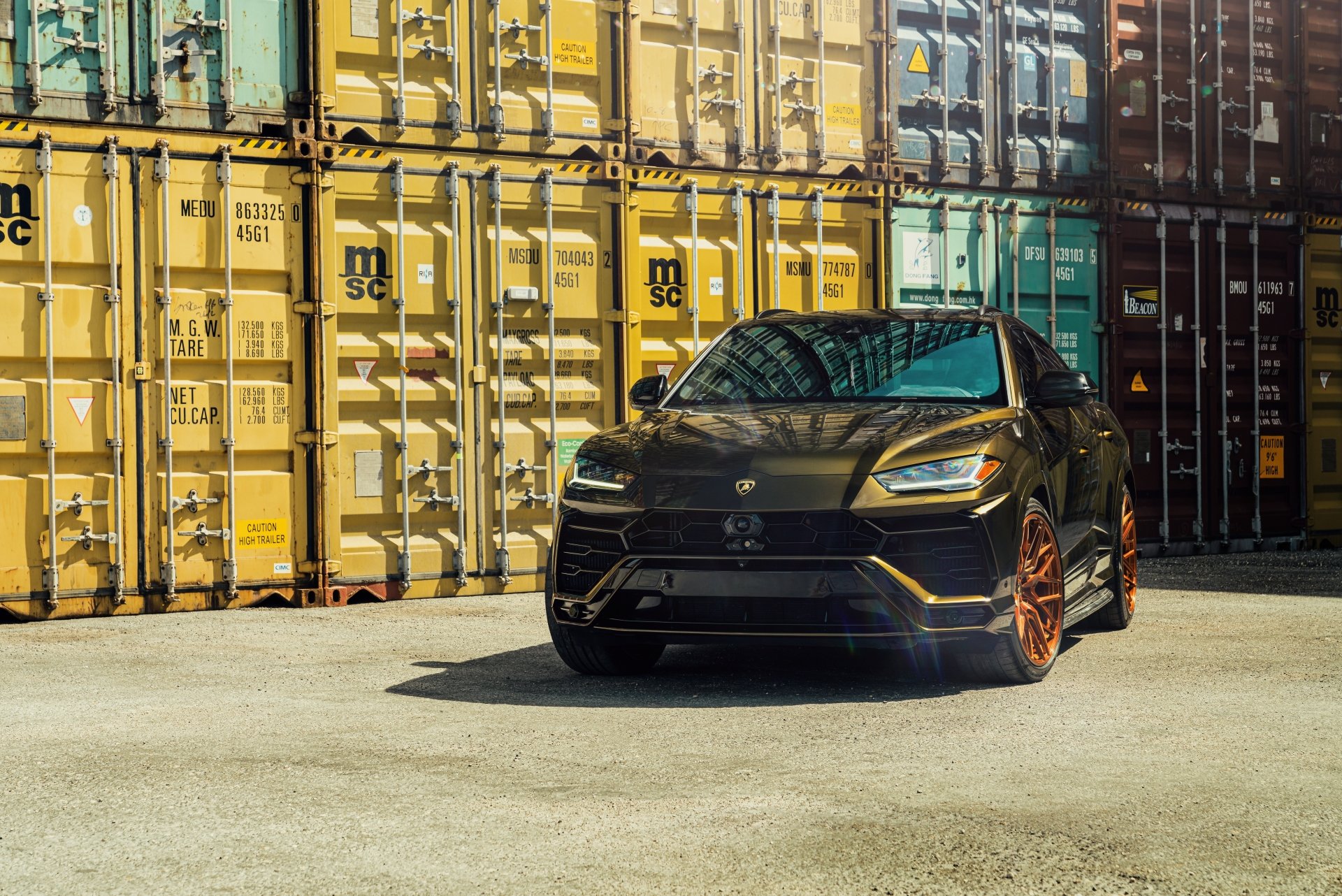 Black Lamborghini Urus SUV parked in front of colorful shipping containers, captured in an 8K Ultra HD PC desktop wallpaper and background.