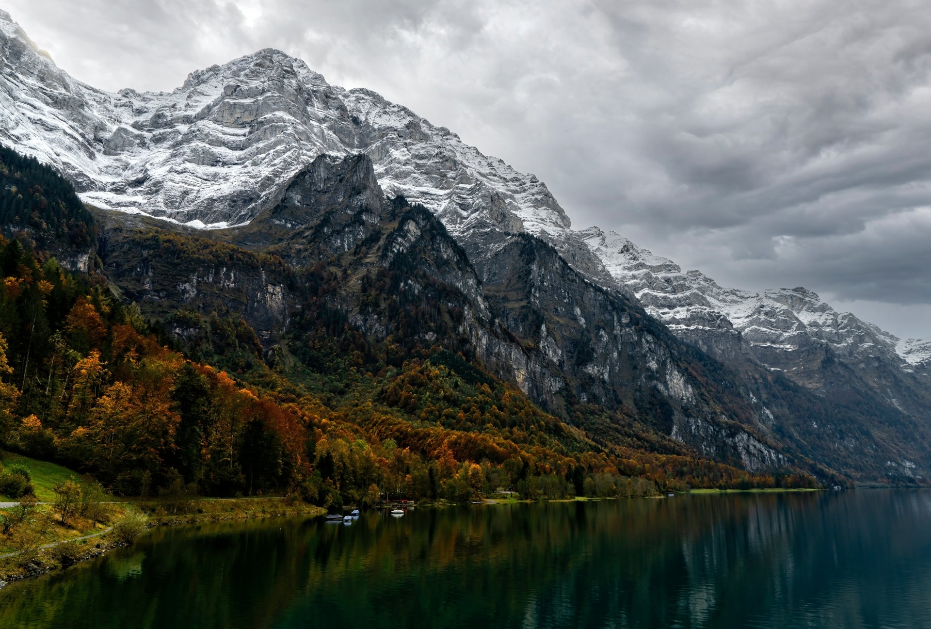 8K Ultra HD nature wallpaper featuring a serene lake reflecting autumn trees and towering snow-capped mountains under a cloudy sky.