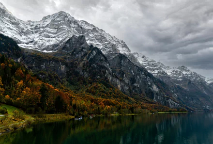 8K Ultra HD nature wallpaper featuring a serene lake reflecting autumn trees and towering snow-capped mountains under a cloudy sky.