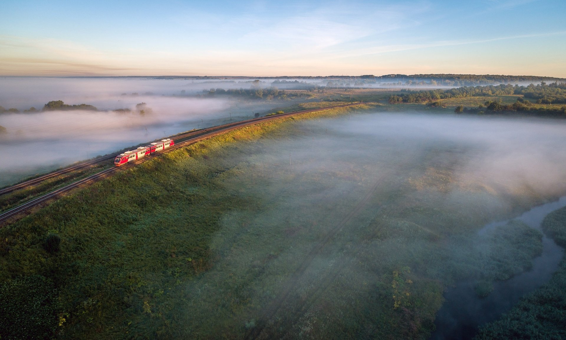 A red train travels through a foggy Russian landscape at sunrise, captured in an HD desktop wallpaper showcasing mist over green fields.