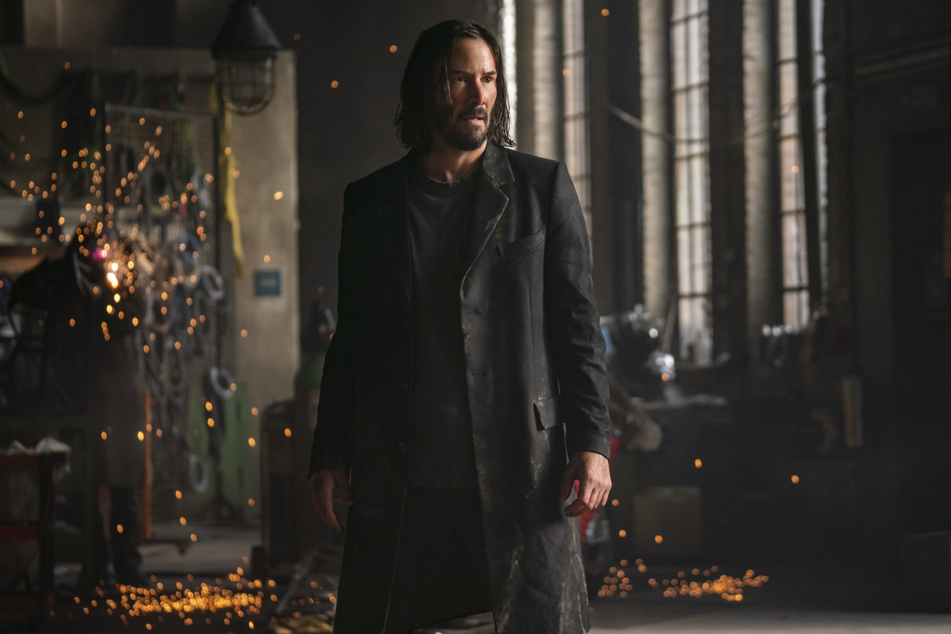 5K Ultra HD desktop wallpaper of a long-haired man in a dark coat amid sparks and tall industrial windows, cinematic scene evoking The Matrix Resurrections.