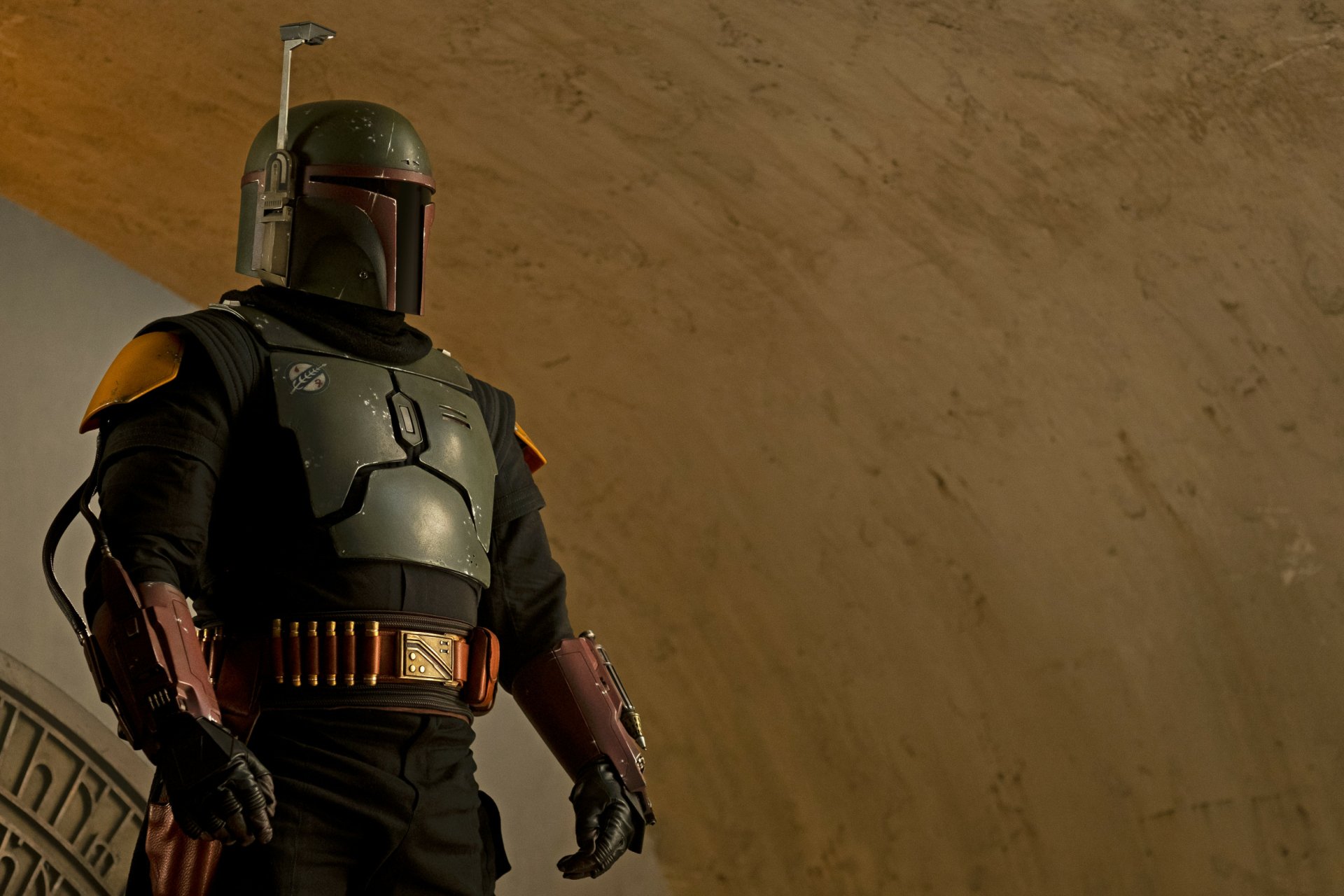 HD PC desktop wallpaper of Boba Fett from the TV show The Book of Boba Fett, standing in full armor under a curved, sandy-hued archway, helmet and blaster visible.
