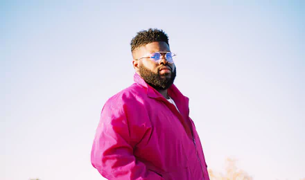 A man in a pink jacket and sunglasses stands against a clear sky, serving as a vibrant HD desktop wallpaper background.