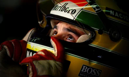 Close-up HD wallpaper of Ayrton Senna wearing his iconic F1 helmet and gloves, capturing his focused expression in a classic motorsport moment.