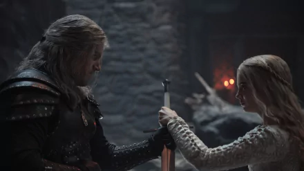 Geralt of Rivia and Ciri from The Witcher clasp a sword in a dim stone hall — moody 4K TV show desktop wallpaper.