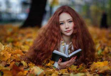 HD PC desktop wallpaper of a redhead model woman with long hair reading a book while reclining amid golden fall leaves, warm autumn tones.
