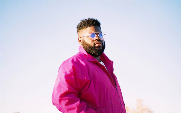 A man in a pink jacket and sunglasses stands against a clear sky, serving as a vibrant HD desktop wallpaper background.