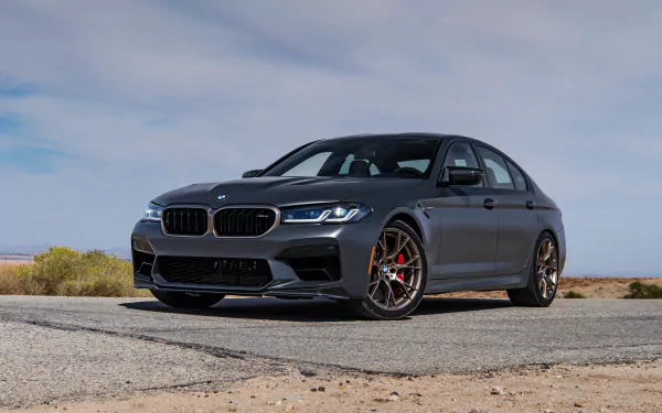 Matte-gray BMW M5 CS parked on an open desert road beneath a cloudy sky — 5K Ultra HD PC desktop wallpaper.
