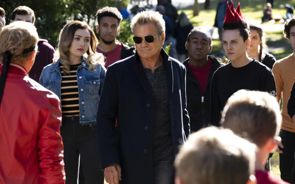 Cobra Kai TV show 2K Quad HD PC desktop wallpaper: a sunglasses-wearing man leads a tense outdoor standoff between rival students.