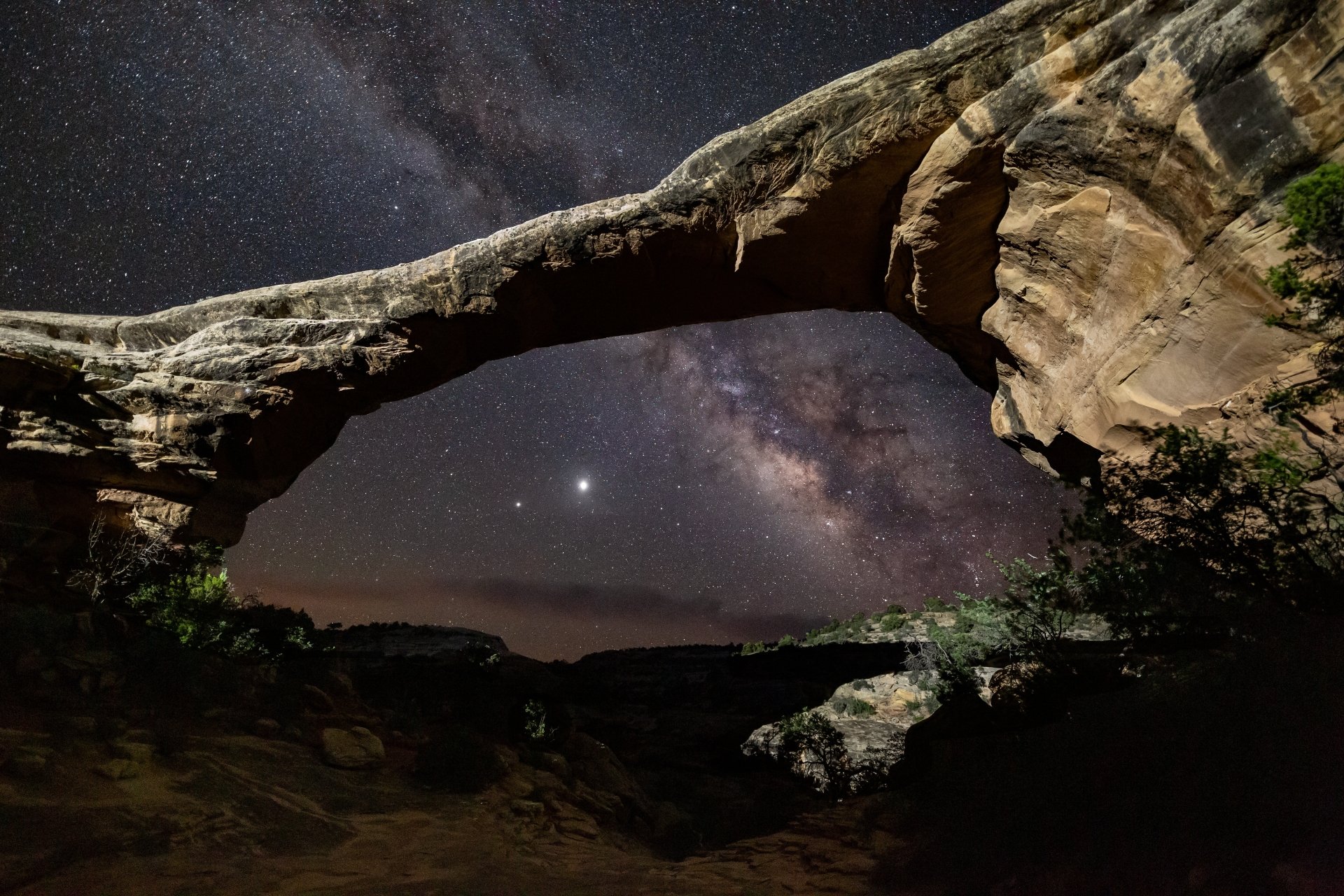 5K Ultra HD PC desktop wallpaper: star-filled night sky and Milky Way framed by a natural stone arch in rugged desert nature.