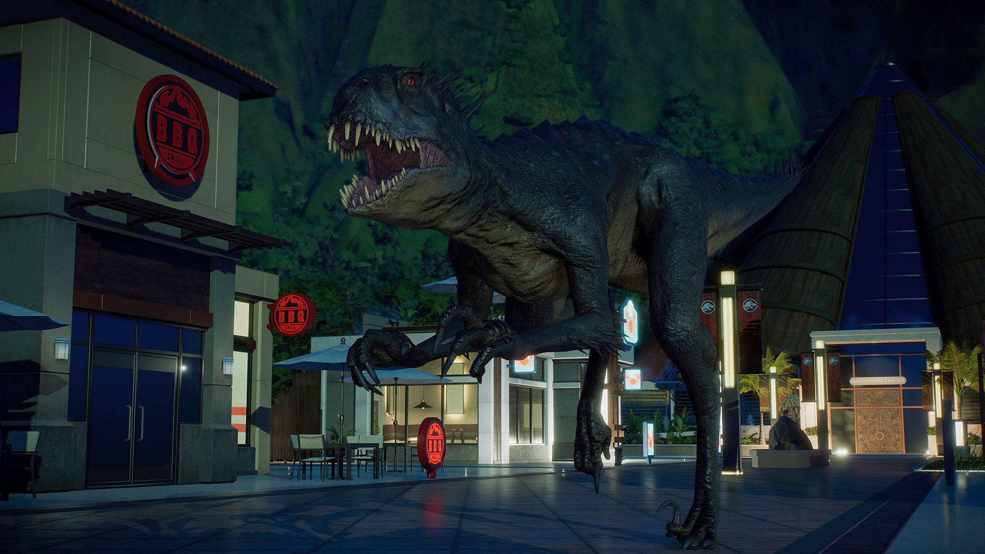 HD PC desktop wallpaper from the video game Jurassic World Evolution 2: a roaring T. rex stalks a rain-slick park walkway between lit buildings at night.