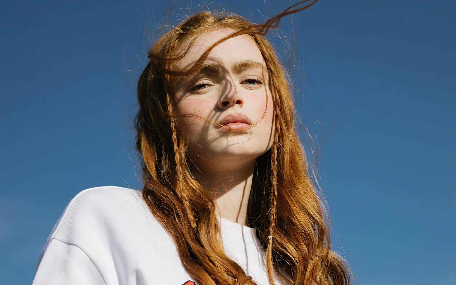 HD desktop wallpaper of redhead celebrity Sadie Sink against a clear blue sky, showcasing her natural beauty and flowing hair.