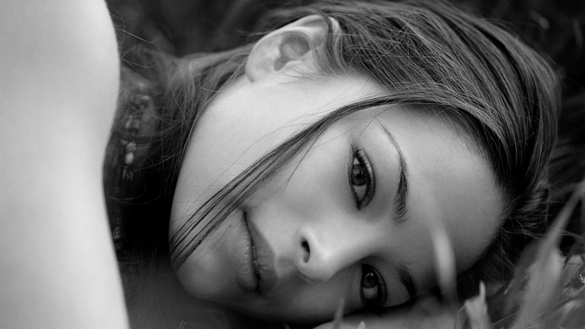 Black and white HD desktop wallpaper featuring a close-up portrait of celebrity Kristin Kreuk lying down with a calm, contemplative expression.