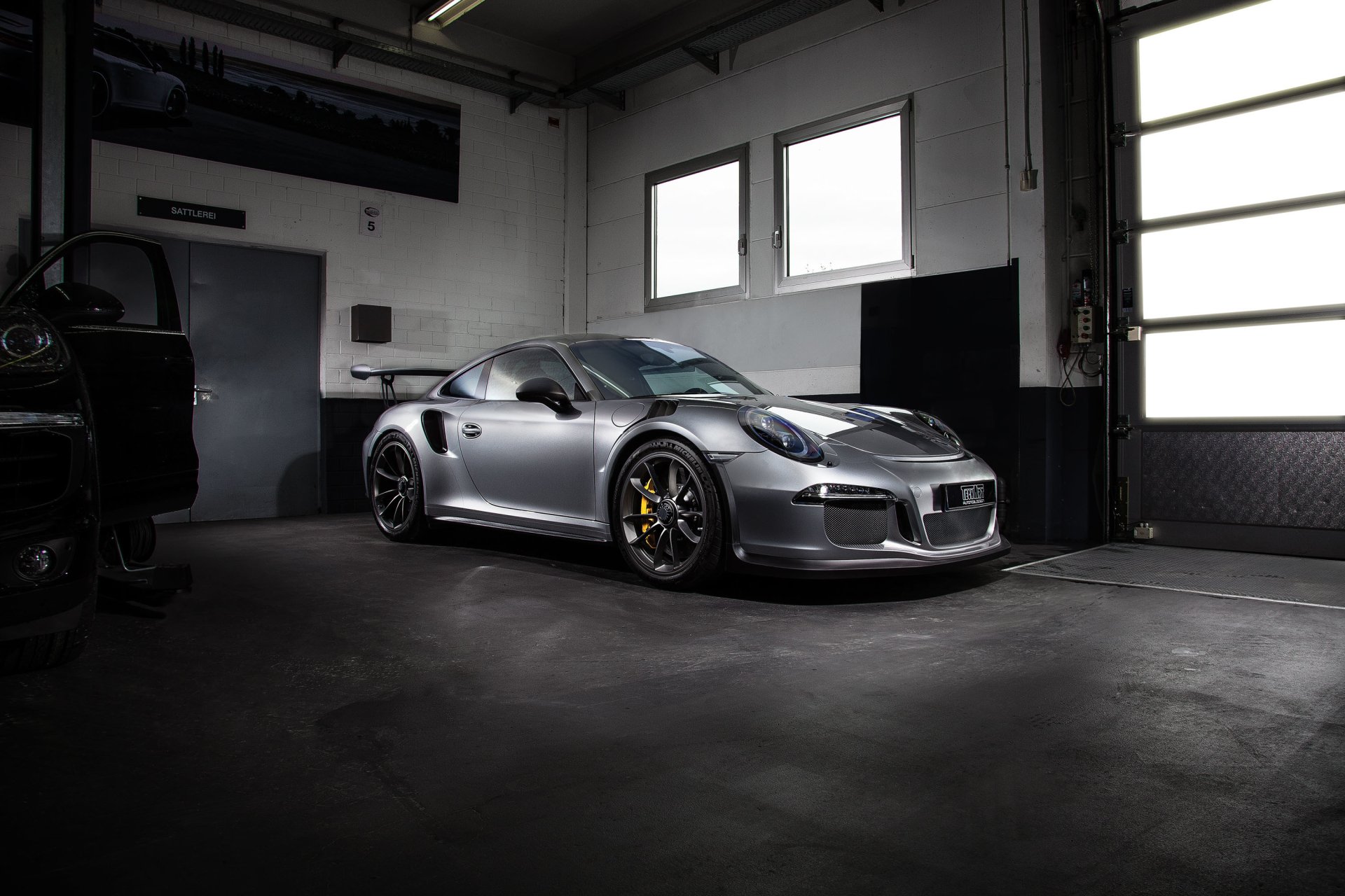 Silver Porsche 911 GT3 parked in a dim industrial garage with dramatic lighting — 2K Quad HD PC desktop wallpaper and background.