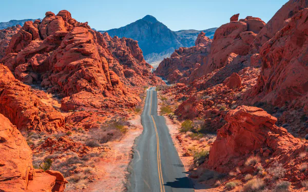 4K Ultra HD PC desktop wallpaper showing a man-made road cutting through vivid red rock formations toward distant mountains under a bright blue sky.