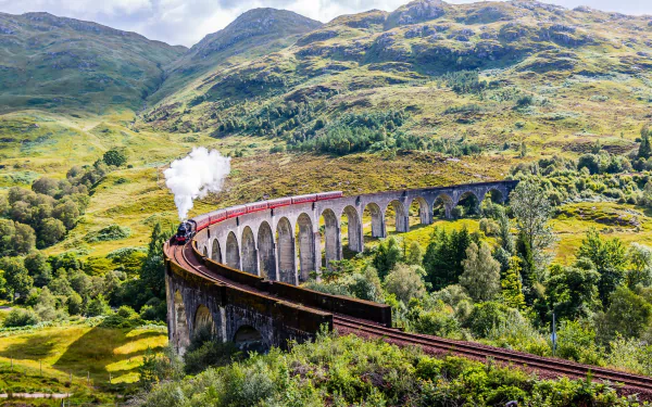 A vintage train crossing a curved viaduct in the lush, green hills of Scotland under a partly cloudy sky, captured in HD for a desktop wallpaper background.