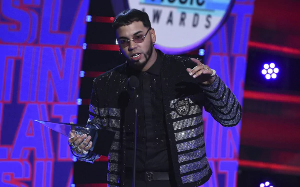 Anuel AA holding an award on stage at a music event, featured in an HD PC desktop wallpaper background.