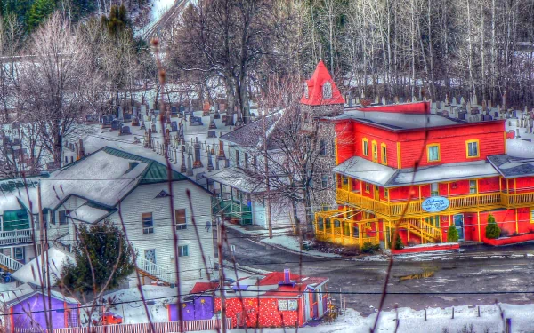 HDR photography 2K Quad HD PC desktop wallpaper featuring a vibrant red-and-yellow house in a snowy village, bare trees and surrounding cottages with high-dynamic-range color and detail.