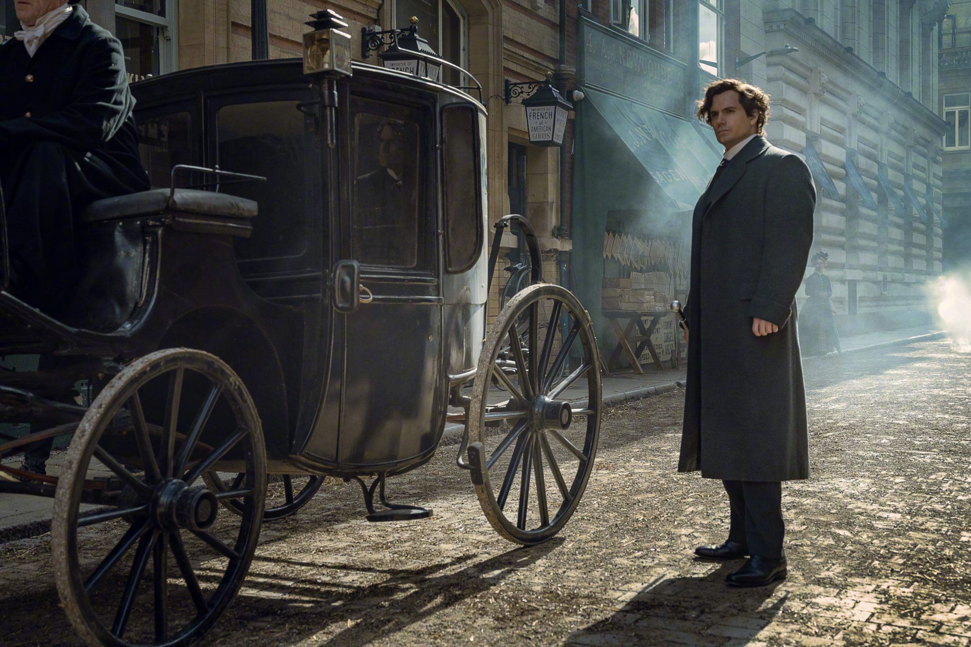 HD desktop wallpaper from the movie Enola Holmes 2: a man in a long dark coat stands beside a horse-drawn carriage on a misty cobblestone street.