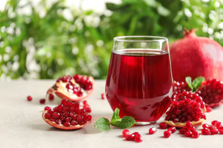 HD desktop wallpaper featuring a glass of vibrant pomegranate juice surrounded by fresh pomegranate seeds and fruit, highlighting rich reds and natural freshness.