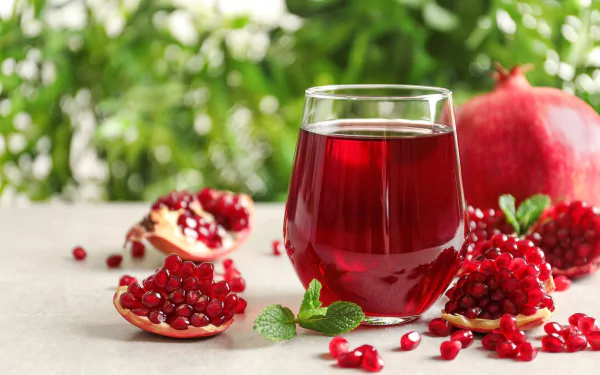 HD desktop wallpaper featuring a glass of vibrant pomegranate juice surrounded by fresh pomegranate seeds and fruit, highlighting rich reds and natural freshness.